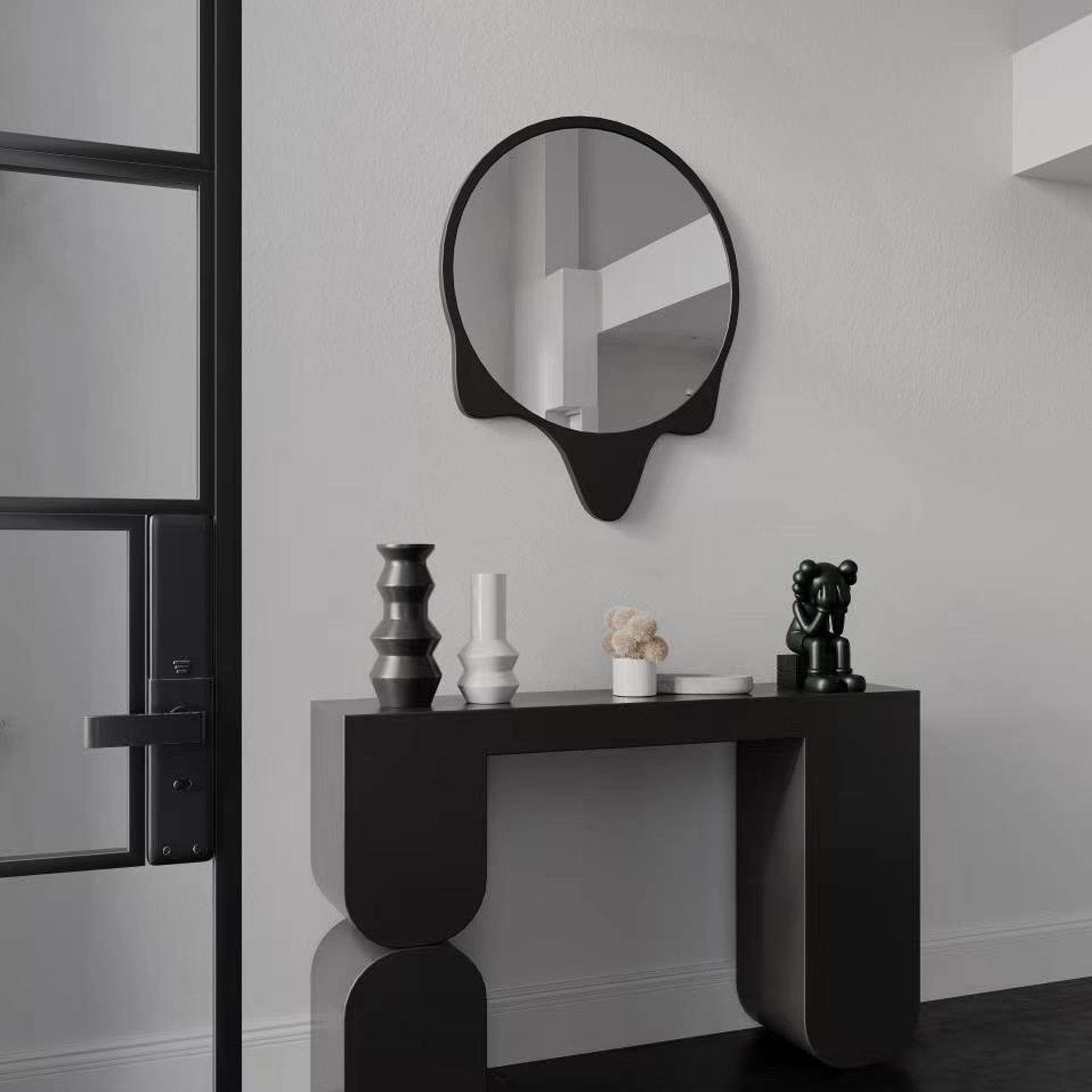 A black round wall mirror with wavy decoration on a black modern entryway table