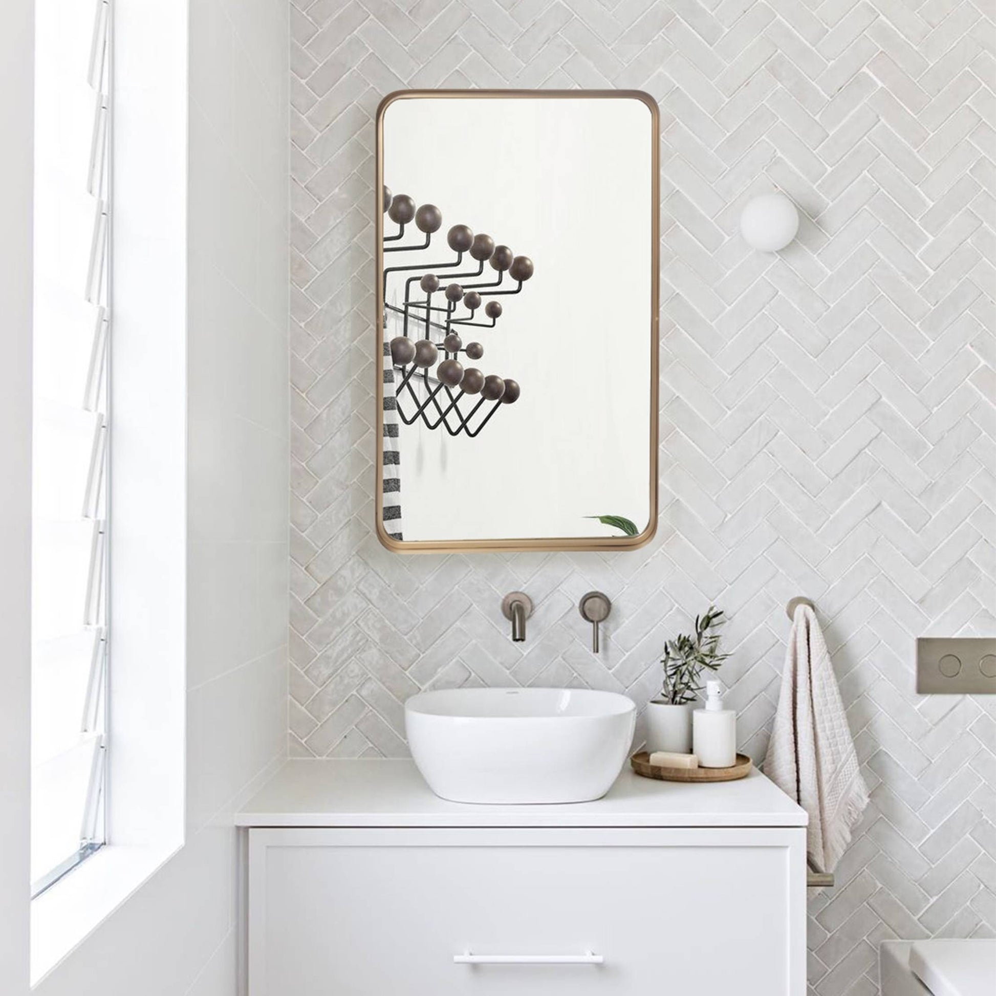 a gold metal rectangular mirror above a white sink in a white-theme bathroom