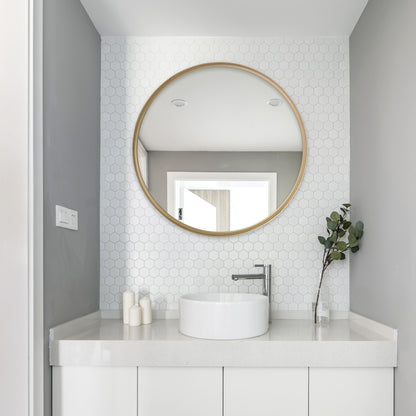 A white-themed bathroom with a white sink and a gold small round  wall mirror